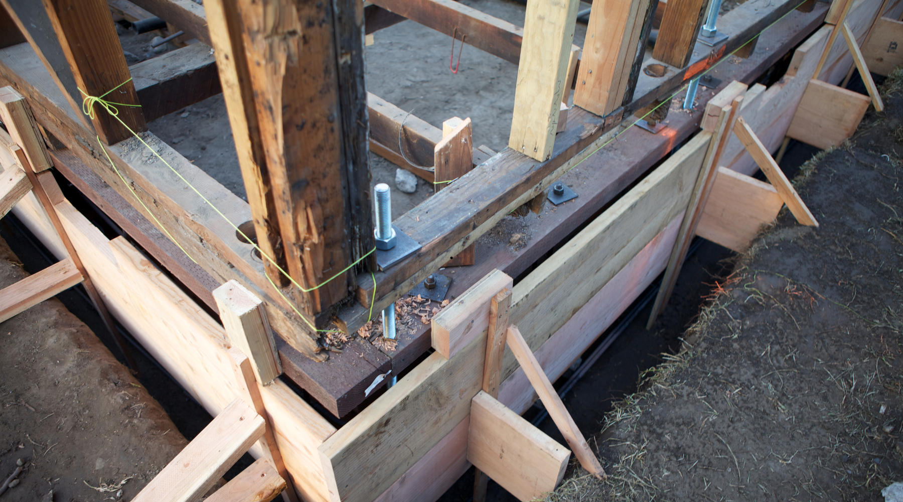 Close-up of house foundation repair with wooden supports, bolts, and framing, showing signs of structural stabilization work